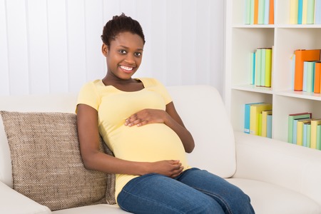 56063952 - happy pregnant woman sitting on sofa at home